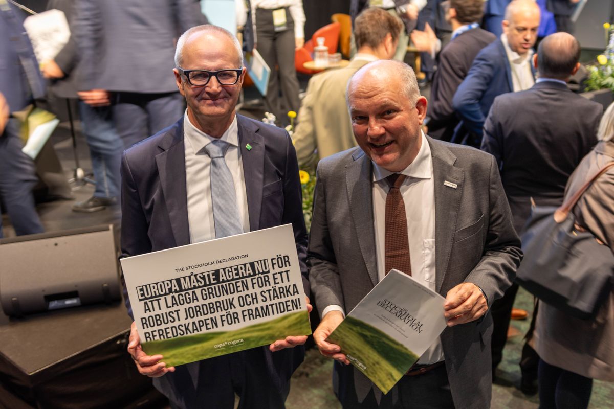 Två män i kostym håller skyltar om europeiskt jordbruk på en konferens
