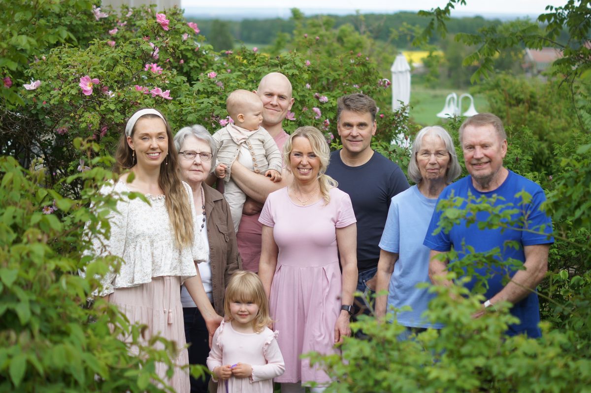 Tre generationer familj poserar tillsammans i grönskande rosenträdgård