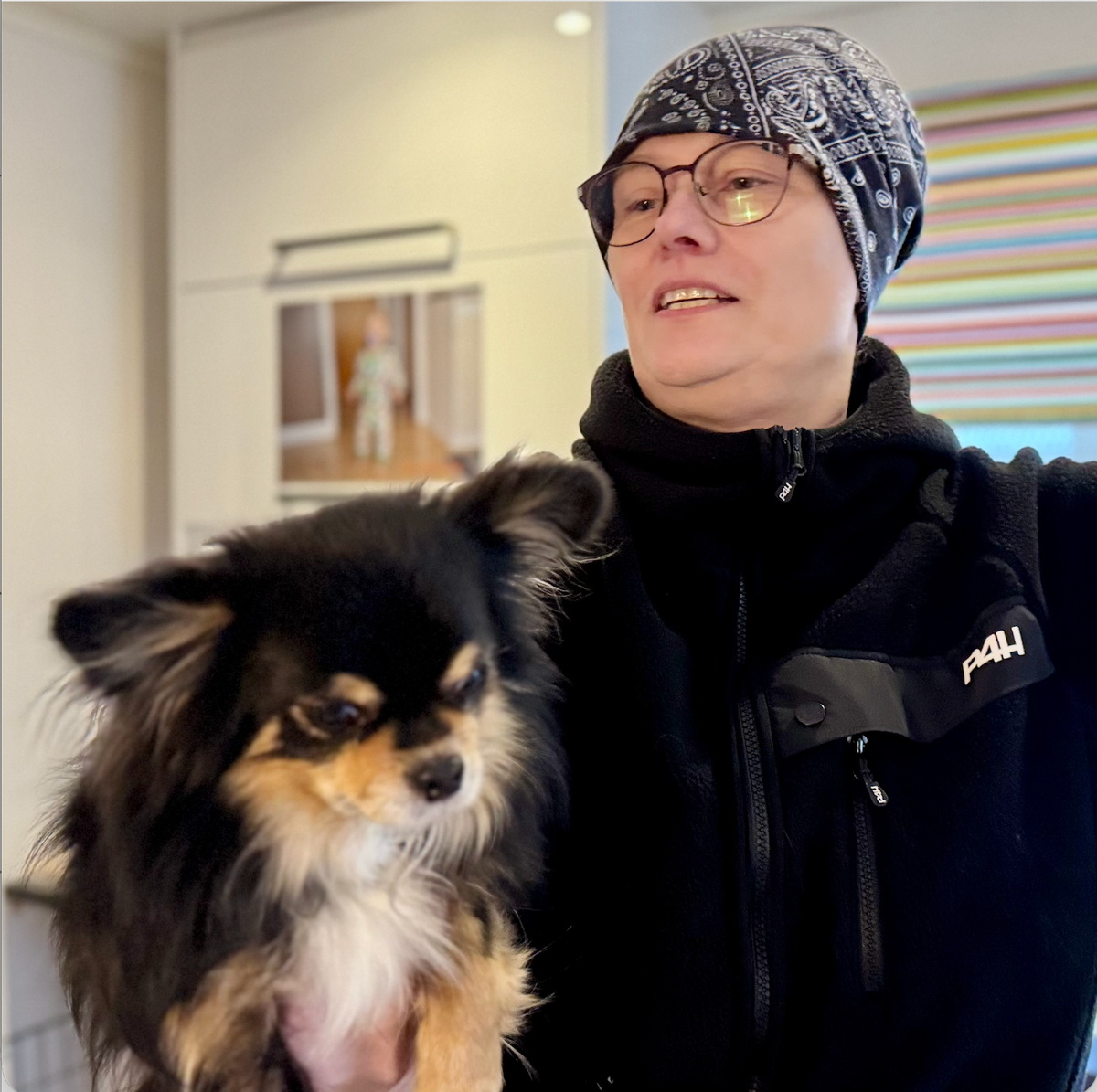 Person med mössa håller en liten långhårig hund inomhus