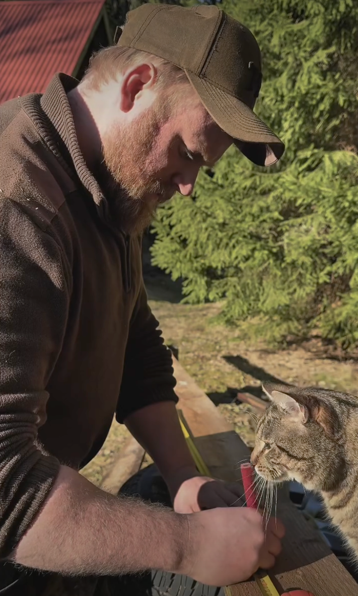Person snickrar utomhus medan en randig katt nyfiket tittar på verktygen