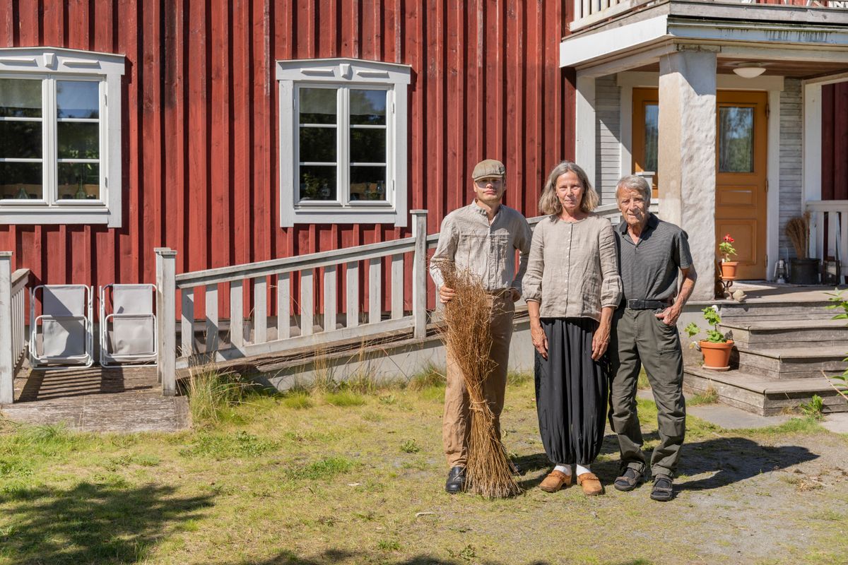 Gustav Karlsryd och hans föräldrar Helena och Tommy står framför ett rött trähus i solsken på gårdsplanen