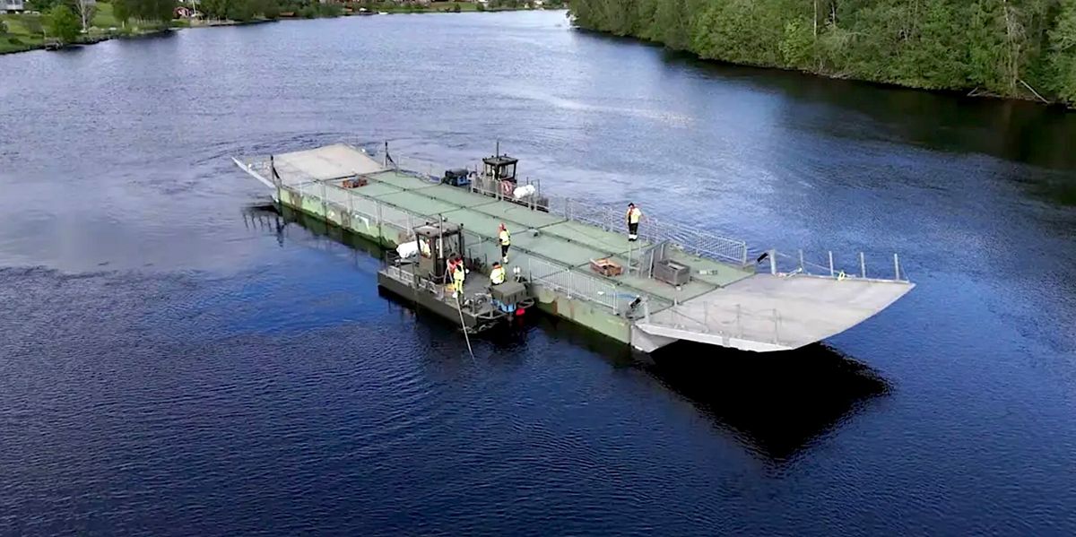 Militär pontonfärja med personal som korsar en lugn flod omgiven av skog