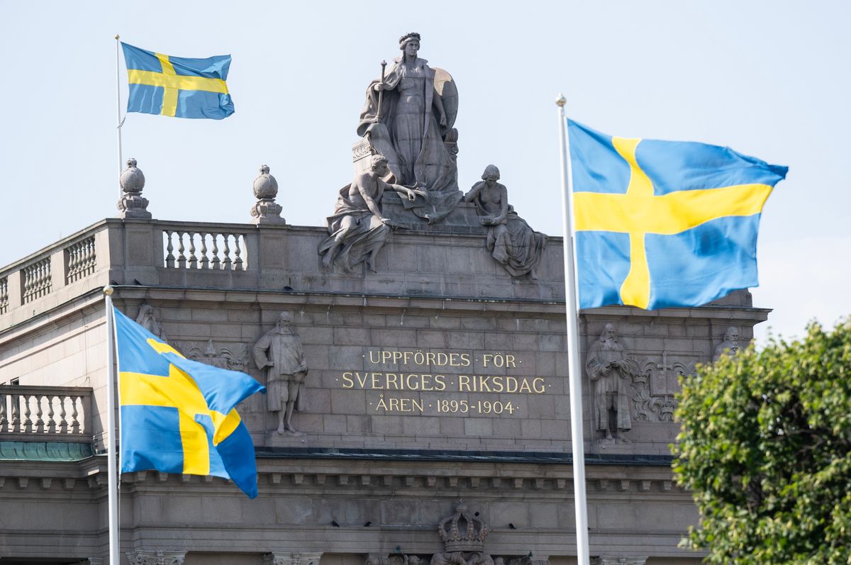 Byggnaden Sveriges riksdag med tre svenska flaggor