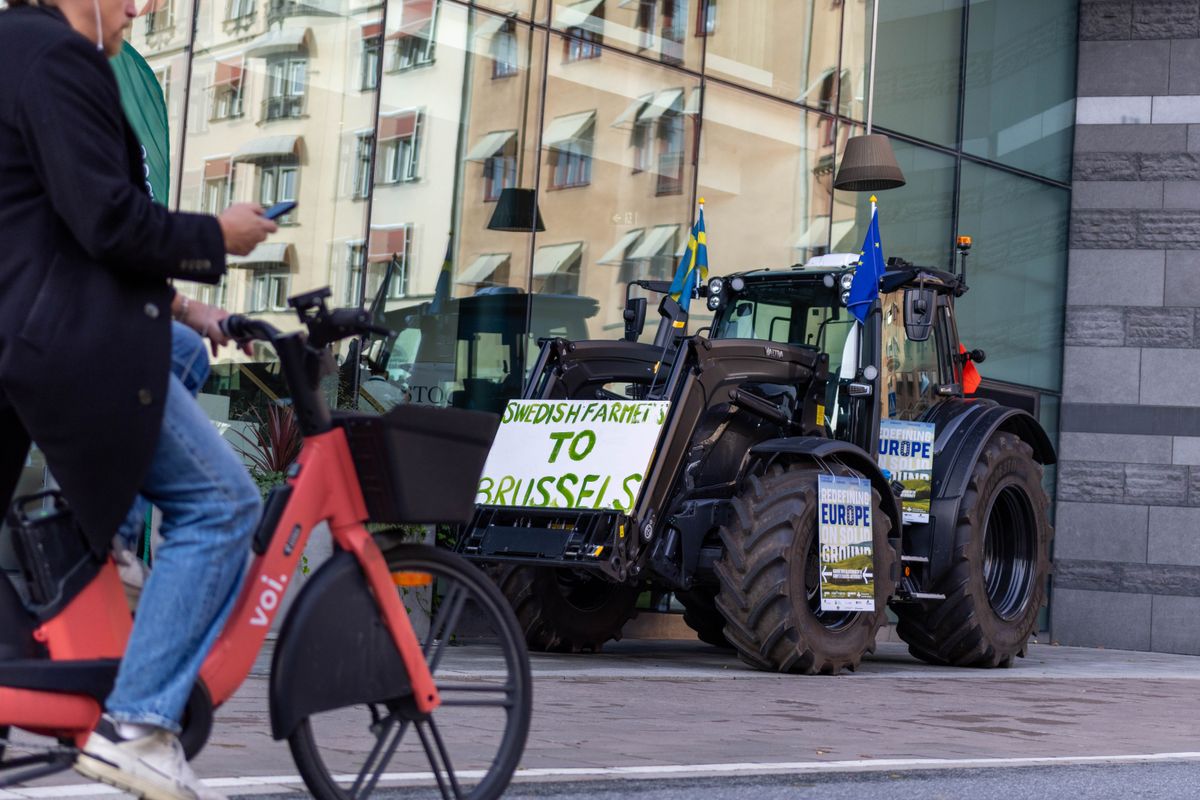 Traktorer med protestskyltar och EU-flaggor parkerade vid glasbyggnad i stadsmiljö