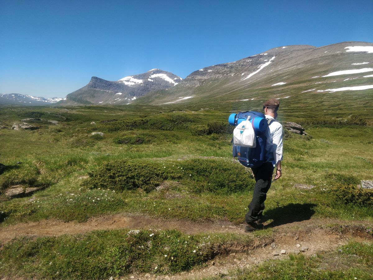 Fjällvandrare i fjällmiljö med skräppåse fastsatt på ryggsäcken