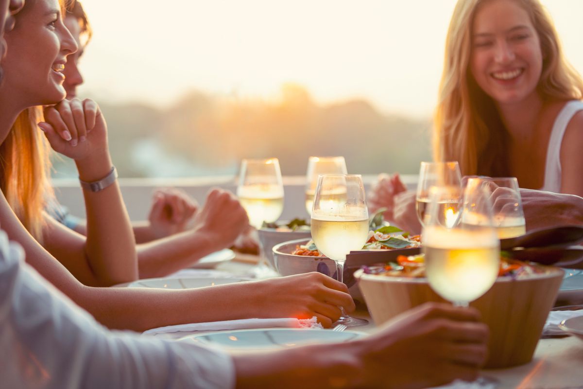 Personer njuter av mat och vin runt ett bord utomhus i kvällssol