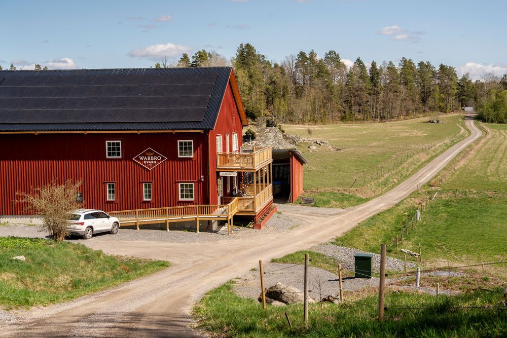 Röd ladugård vid grusväg på landet, med parkerad vit bil och öppna fält