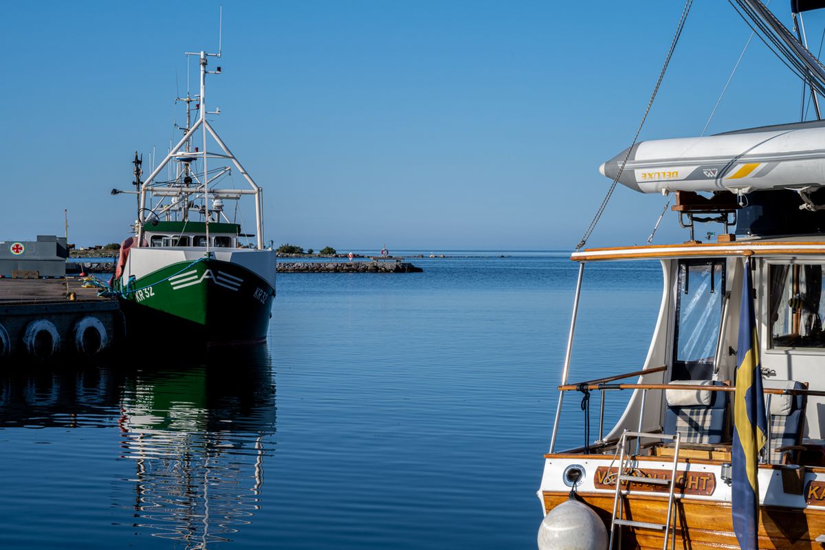 Fiskebåt och segelbåt i lugn hamn med klar blå himmel