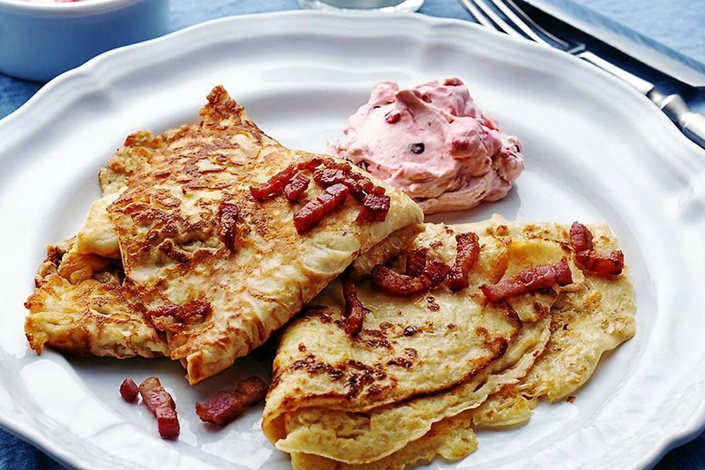 Pannkakor med knaperstekt bacon och rosa bärkräm på vit tallrik