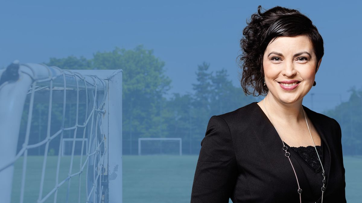 Leende Terese Bengard i svart kavaj framför suddig fotbollsplan och målbur