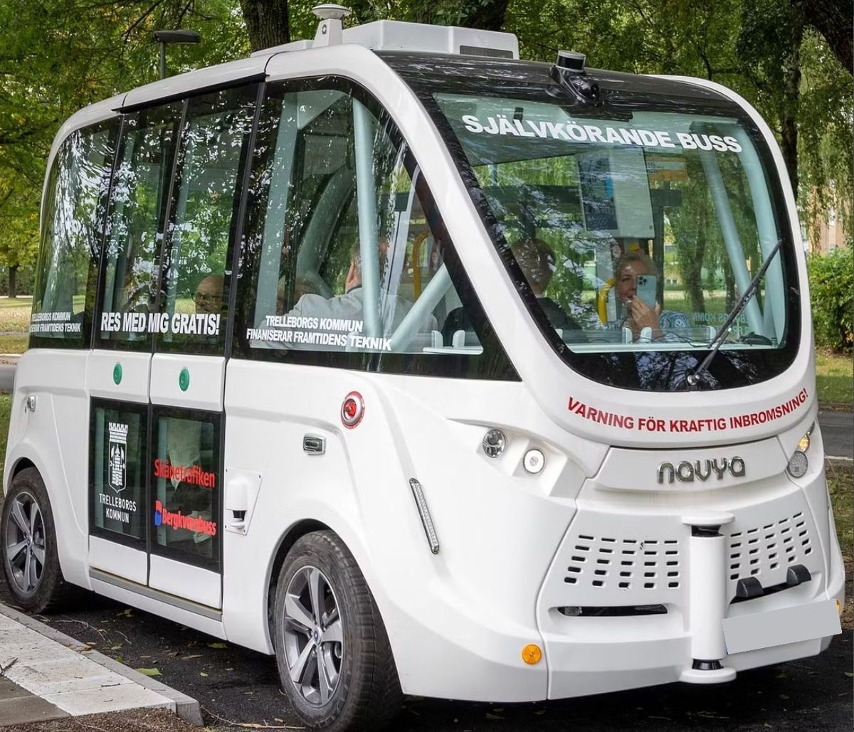 Vit självkörande småbuss körs i stadsmiljö med passagerare ombord