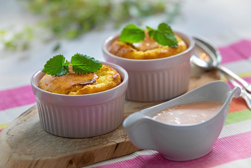 Två ugnsbakade desserter i vita formar med citronmeliss och sås vid sidan