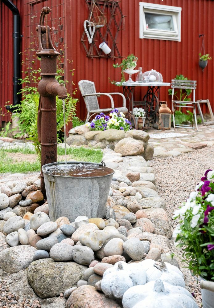 Kreativt återbruk har förvandlat en rostig pump och en gammal hink till ett vattenspel som porlar rofyllt. Fint inramat med lösa, runda stenar.