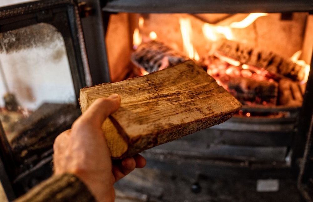 Person ur bild matar in vedträ i kamin.