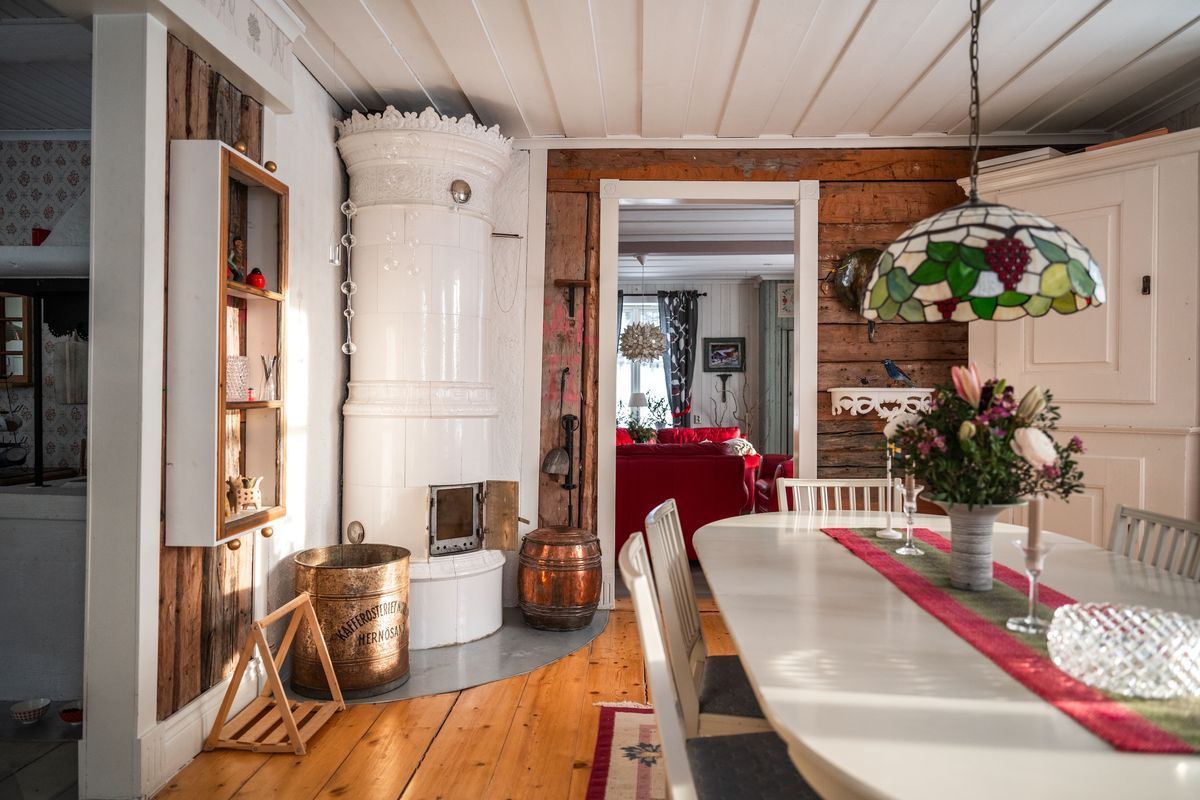 Lantligt kök med kakelugn, träväggar, matbord och utsikt mot rött vardagsrum
