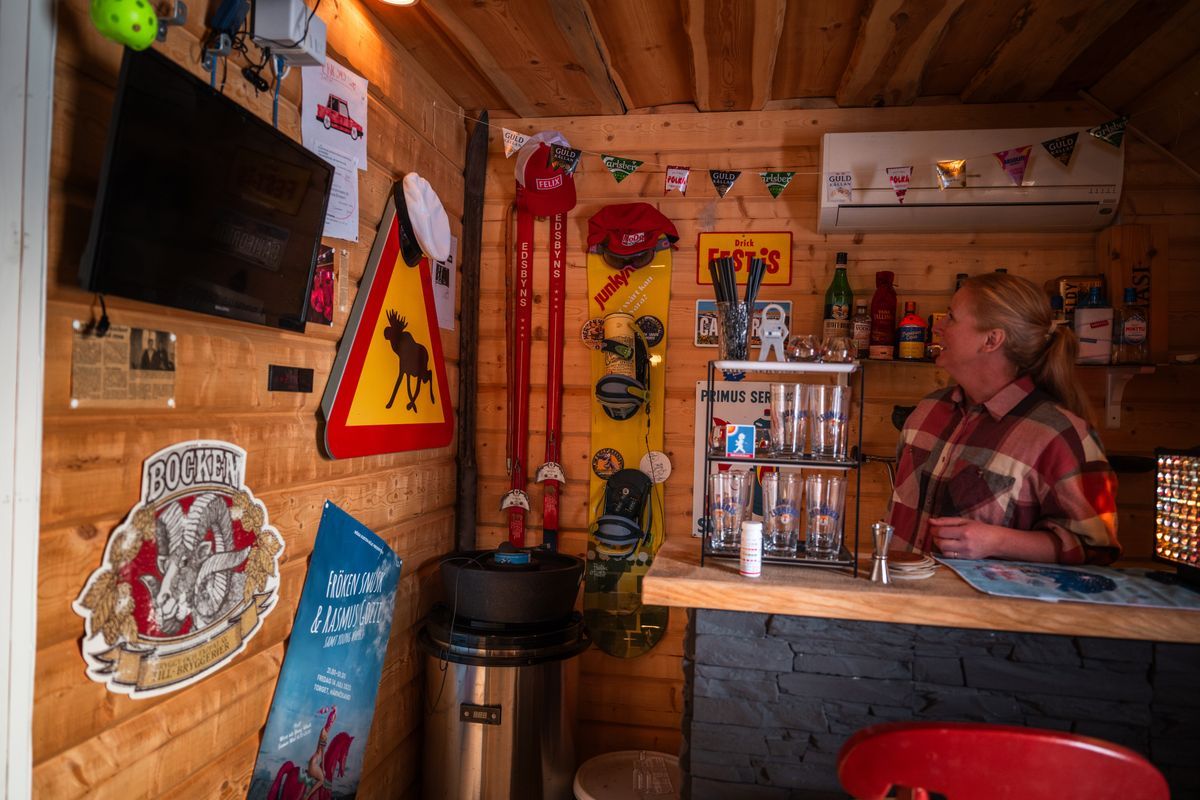 Eva-Karin i liten hemmabar med träväggar, tv och färgglada öl- och vägskyltar.