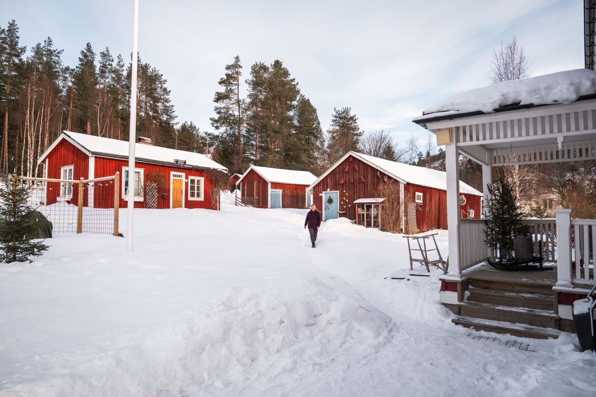 Snötäckt gård med röda stugor och Eva-Karin som går mellan husen