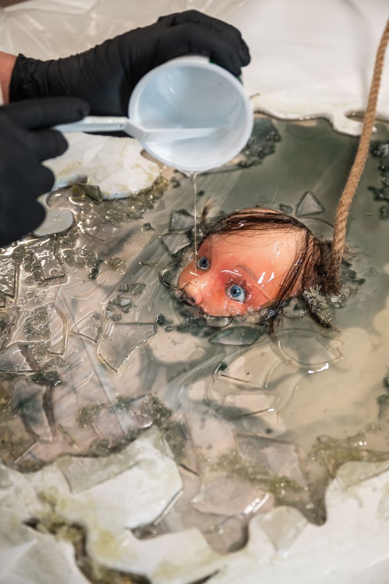 Dockhuvud nedsänkt i vätska medan en person med handskar häller mer ovanpå