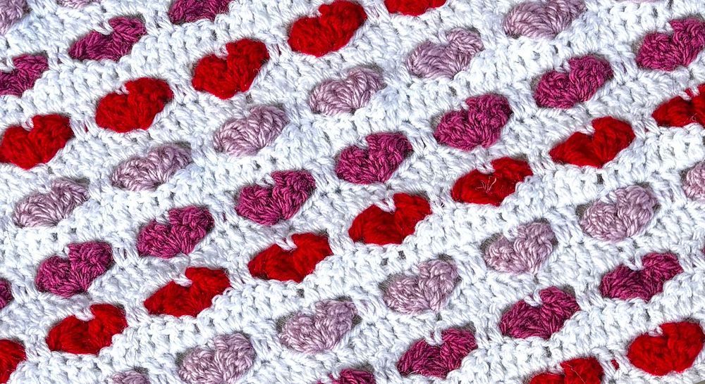 Virkad duk med rosa och röda hjärtan på vit bakgrund.