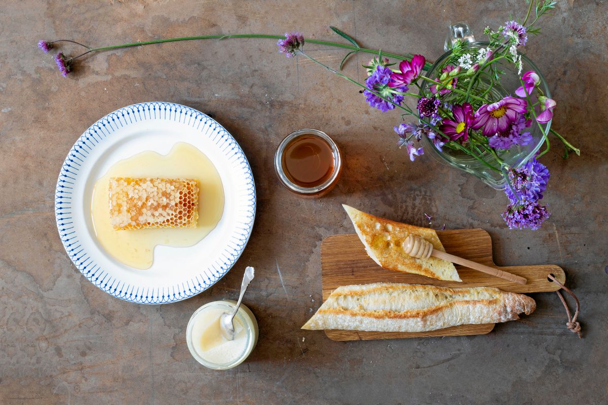 Honungskaka, baguette med honung och vas med färska blommor på bord