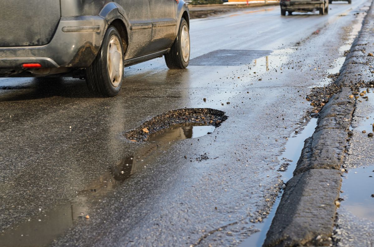 Bil kör förbi ett stort potthål på en blöt och skadad asfaltväg