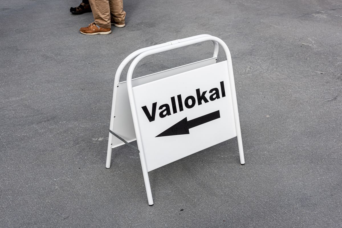 Vit trottoarskylt på asfalt med texten ”Vallokal” och pil som visar vägen