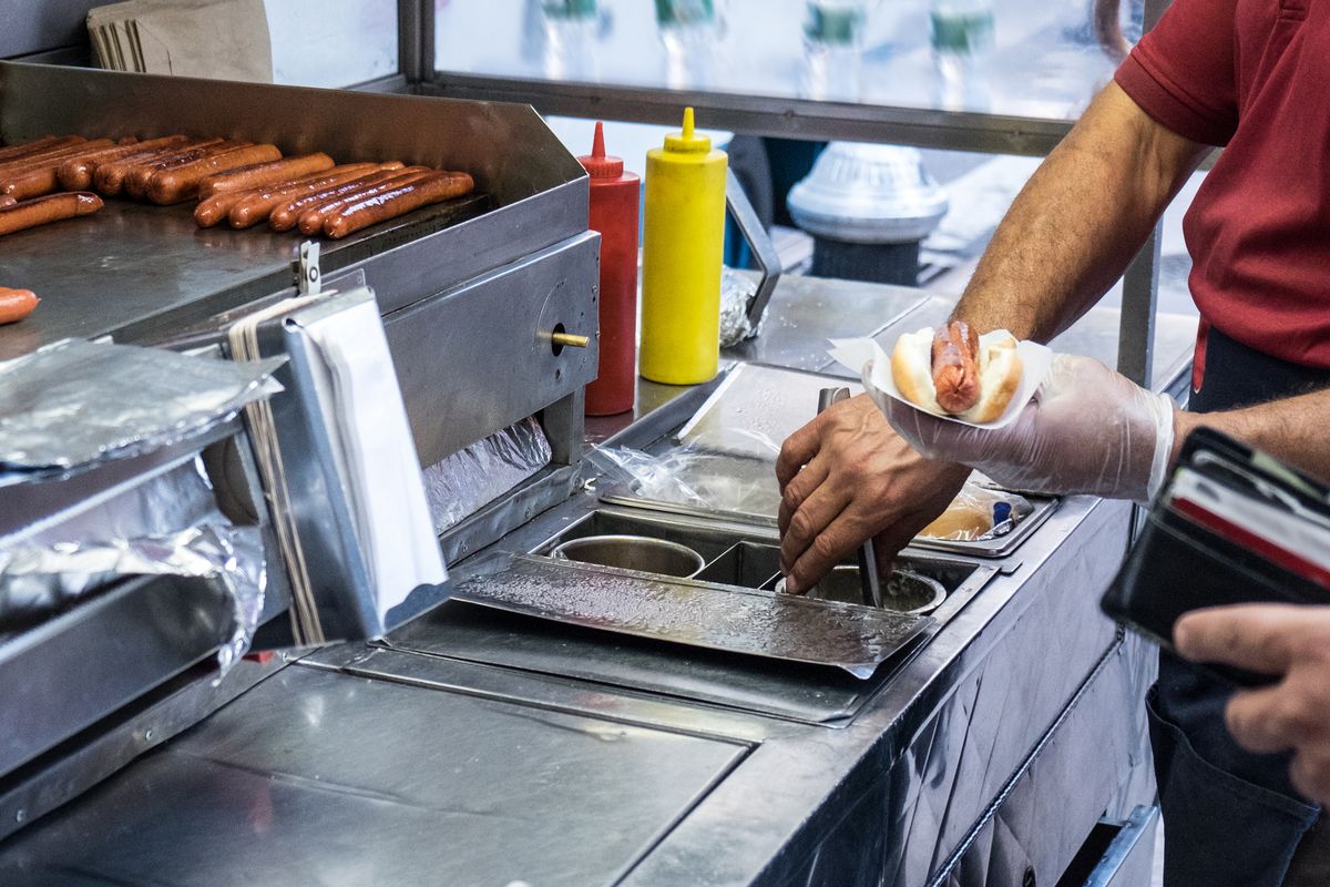Korvvagn med grillade varmkorvar och hand som förbereder korv med bröd