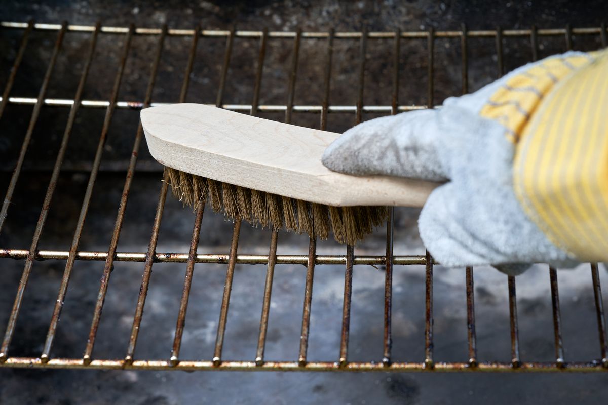 Hand med grillborste rengör ett smutsigt grillgaller utomhus