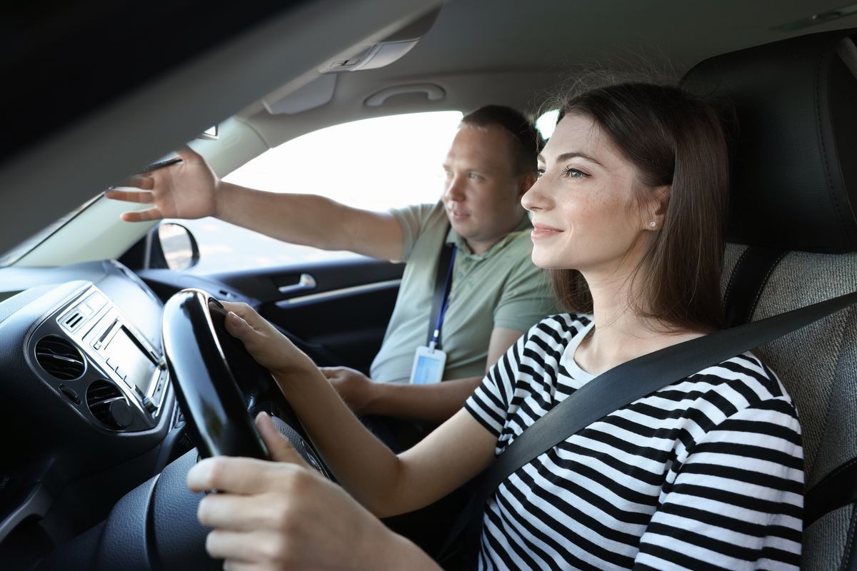 Ung kvinna kör bil medan en handledare ger instruktioner i passagerarsätet