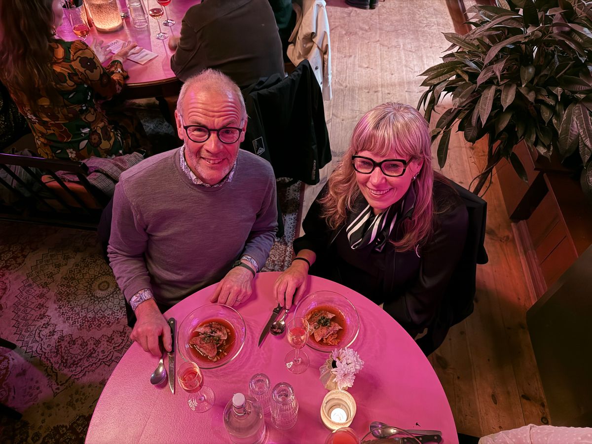 Två personer sitter vid ett rosa bord och äter middag i mysigt restaurangljus