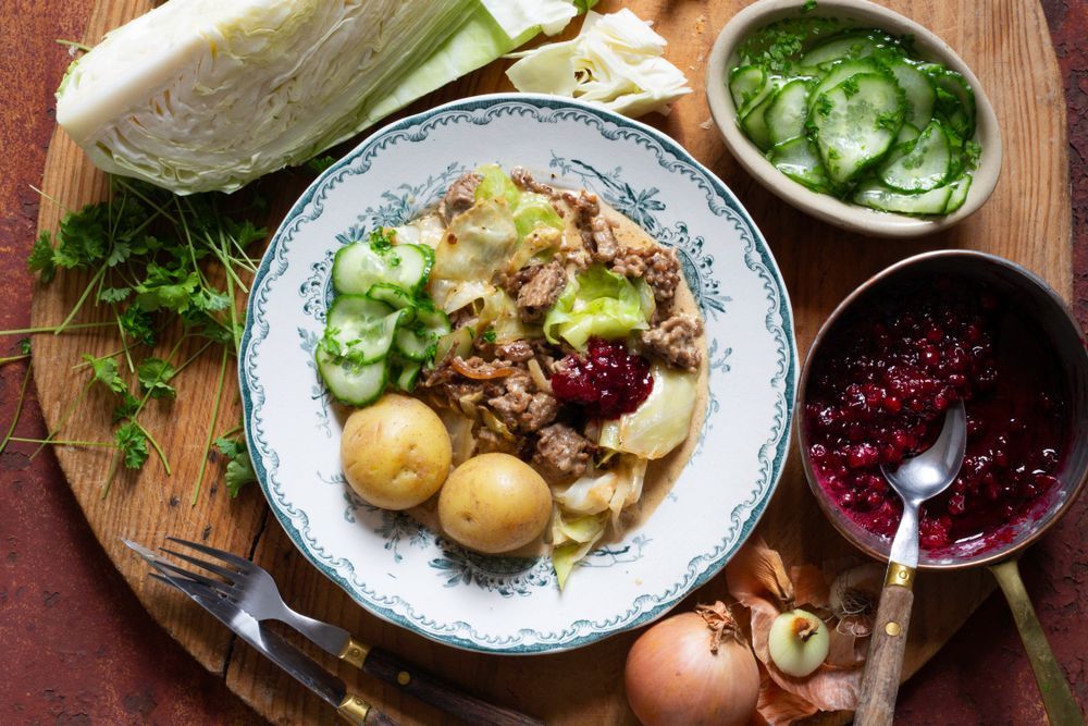 Kålmaja med kokt potatis, inlagd gurka och lingonsylt på porslinstallrik.