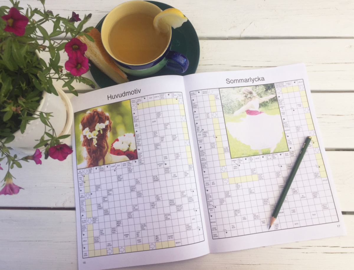 Uppslagen korsordstidning på vit uteplats med kopp te, blommor och penna
