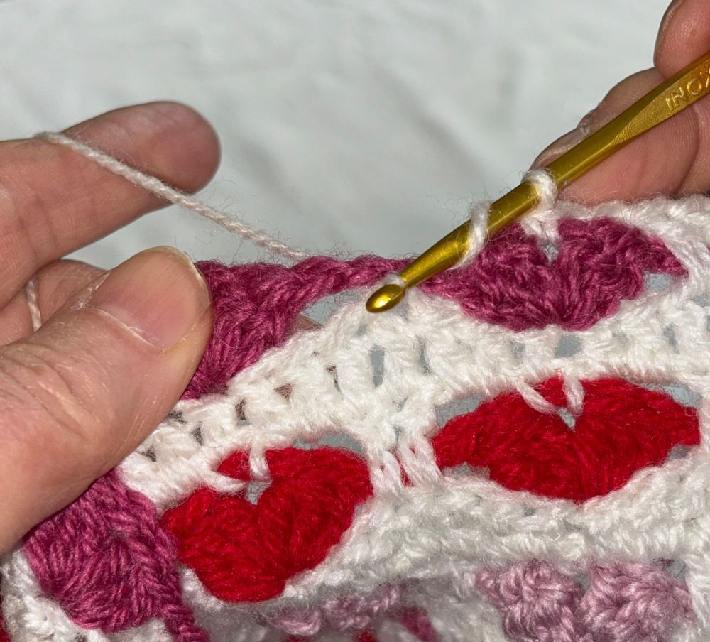 Händer virkar med rosa och rött garn.