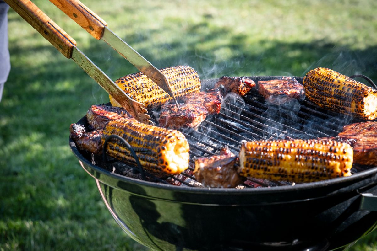 En person grillar kött och majskolvar.