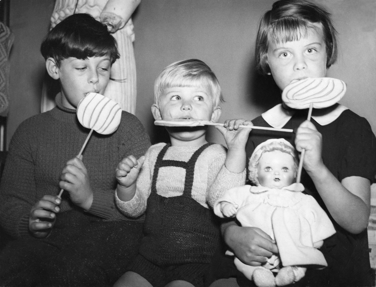 Tre barn i rad, syskonen Per-Evert, Sven-Bertil Ellinor med slickepinnar; Ellinor håller en docka i knät