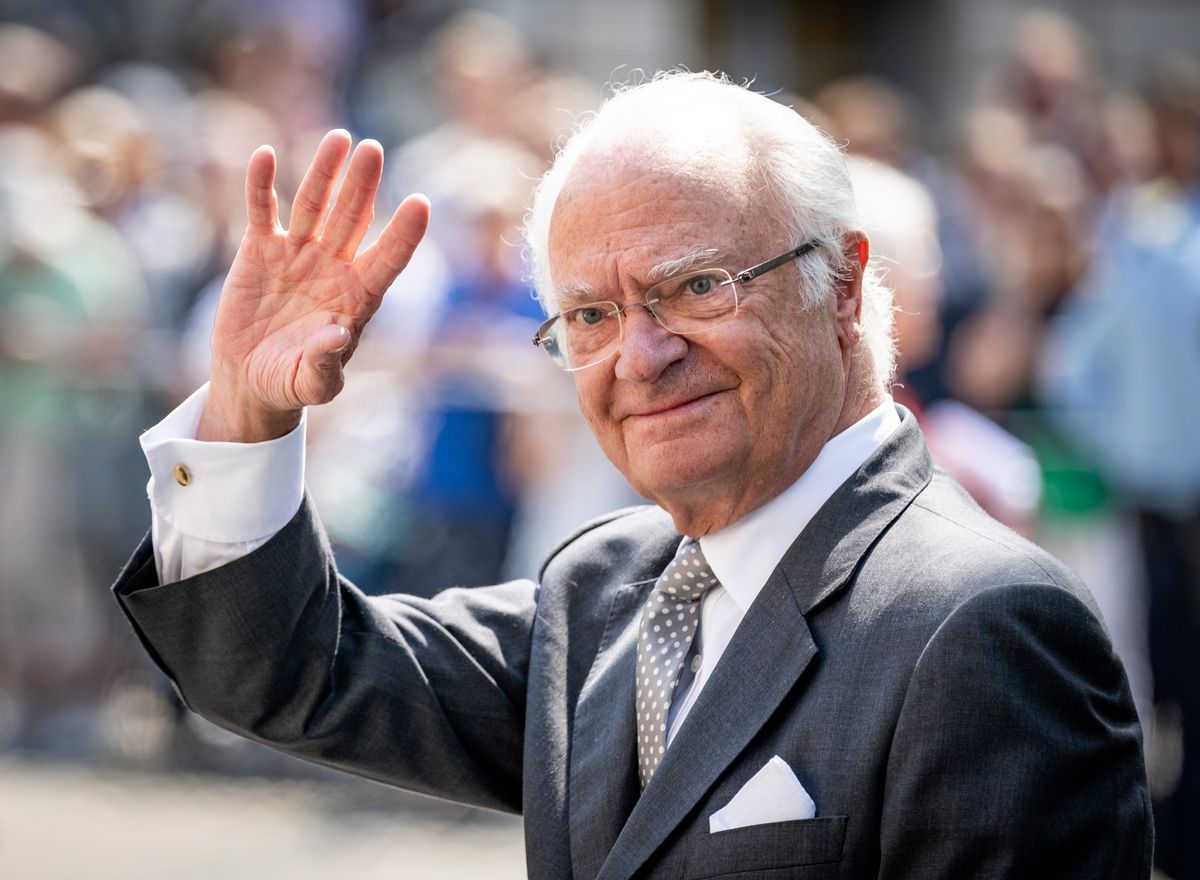 Leende kung Carl XVI Gustaf i kostym och slips, vinkar mot åskådare