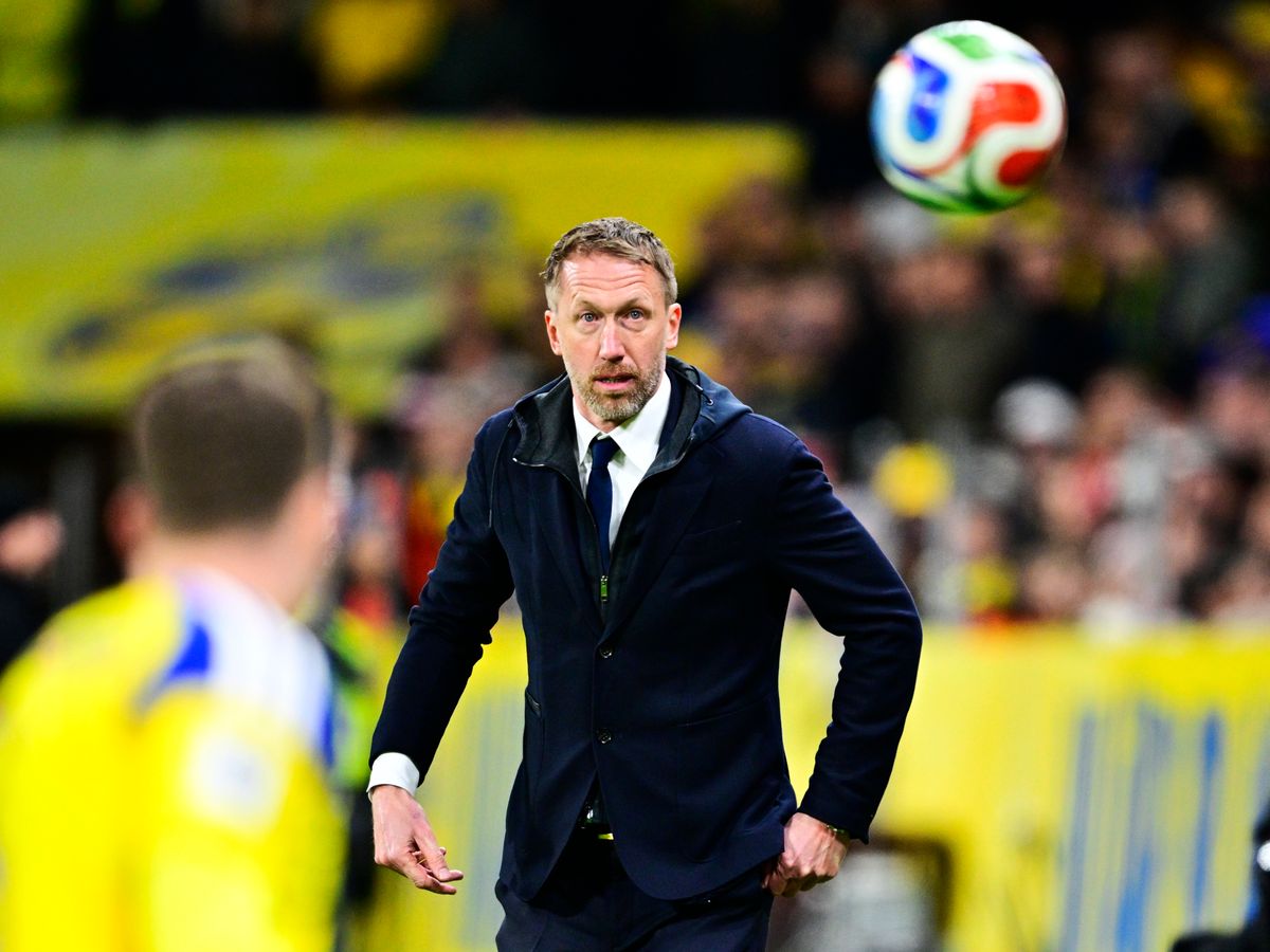 Fotbollstränare Graham Potter på sidlinjen följer bollen i luften under match. Spelare i gulblå matchtröja suddigt i förgrunden.