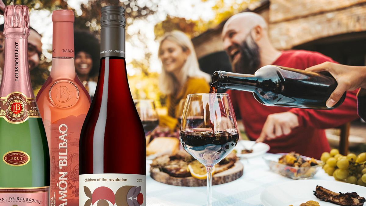 Vinflaskor i förgrunden framför en utomhusmiddag där personer skrattar och vin hälls upp i glas.