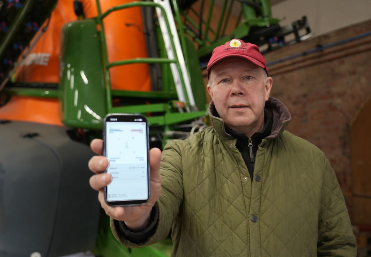 Man i lada visar en mobilskärm med app framför stor grön jordbruksmaskin