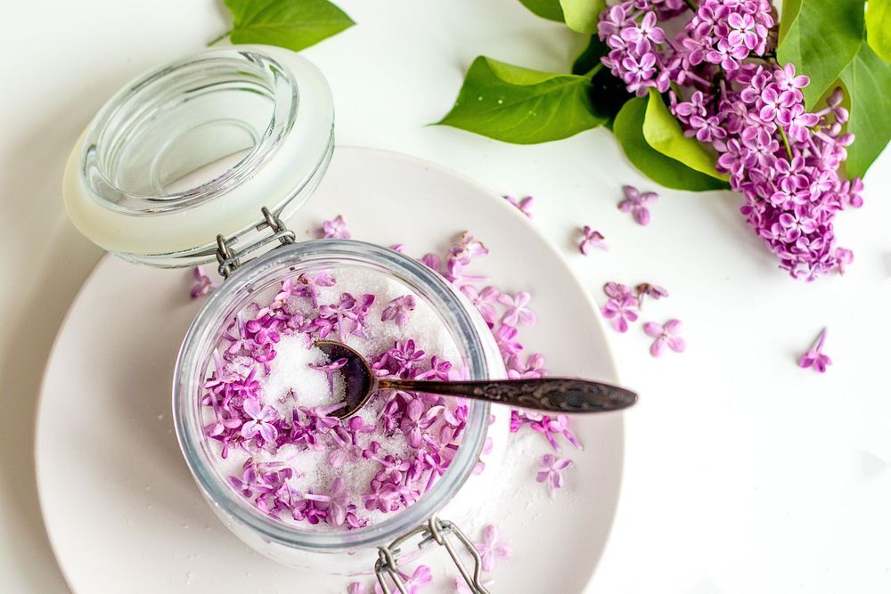 Glasburk med socker och syrenblommor står på vit tallrik.