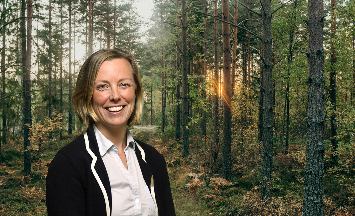Leende kvinna framför solbelyst skogsstig