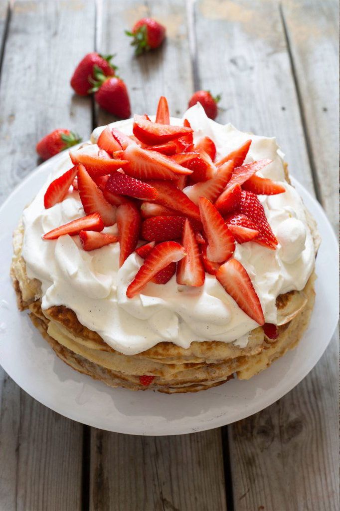 Pannkakstårta med grädde och jordgubbar på tallrik.