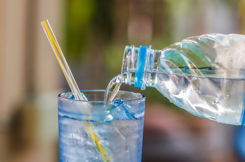 Vatten på flaska som hälls i sugrörsförsett glas.